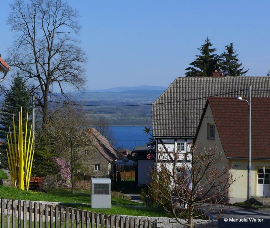 Das Foto von Manuela Walter, eingereicht zum Markersdorfer Fotowettbewerb 2016, zeigt die Ortmitte des heutigen Markersdorfer Ortsteils Jauernick-Buschbach mit Goldner Ähre, Berggasthof und Blick auf den Berzdorfer See, den zweitgrößten See in Sachsen.